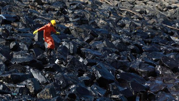 An emergency worker walks amidst oil deposits as he cleans oil from the shoreline of Ennore Port following a collision between two oil tankers, in Chennai, India. (REUTERS)