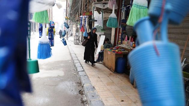 A Syrian woman walks past brooms and plasticware. (Abd Doumany/AFP)