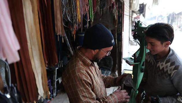 A Syrian cobbler inspects a shoe handed to him by a young boy in Douma. (Abd Doumany/AFP)