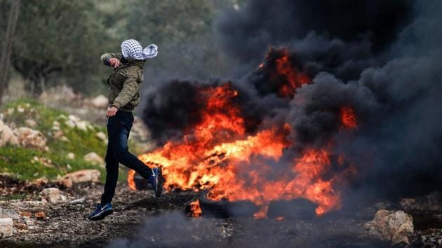 A Palestinian protester hurls stones at Israeli security forces, near a fire during clashes following a weekly demonstration against the expropriation of Palestinian land by Israel in the village of Kfar Qaddum, near Nablus, in the occupied West Bank on February 17, 2017. (JAAFAR ASHTIYEH / AFP)