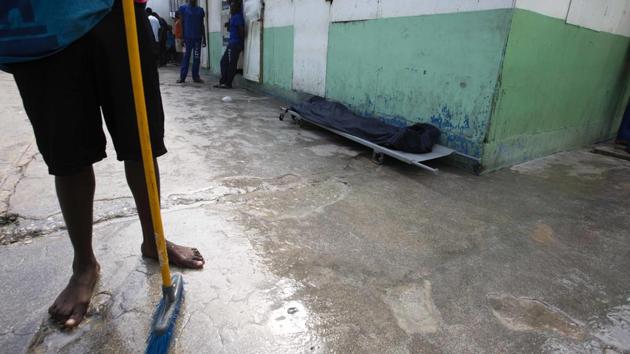 A prisoner stands near the body of an inmate, covered with a plastic tarp, who died of malnutrition. (Dieu Nalio Chery/AP)