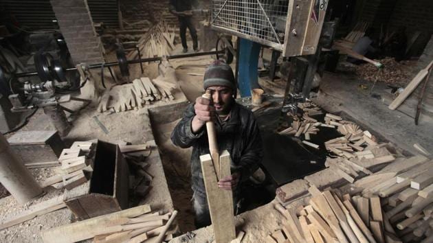 A worker fits a handle into a spliced bat. Each craftsman at the site refines up to 100 bats a day, chiselling and planing the wood into the shape of a bat before the handle is attached. (Waseem Andrabi / HT Photo)