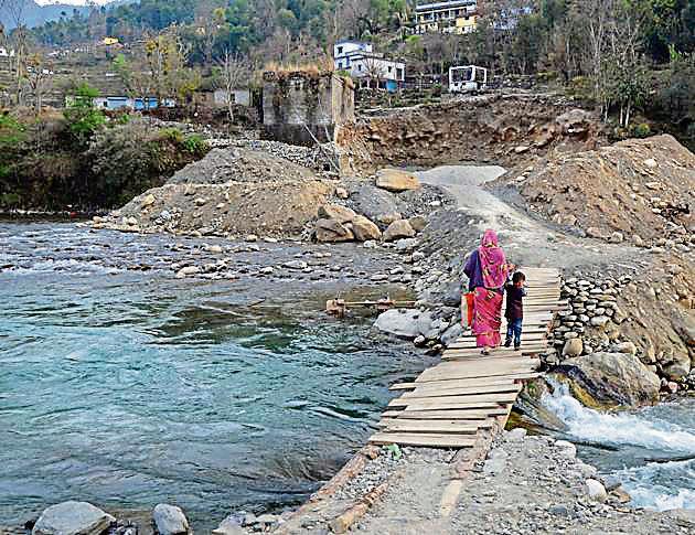 A woman and her child walk across a temporary wooden structure to cross the Pindar river. (HT Photo) A woman and her child walk across a temporary wooden structure to cross the Pindar river. (HT Photo)