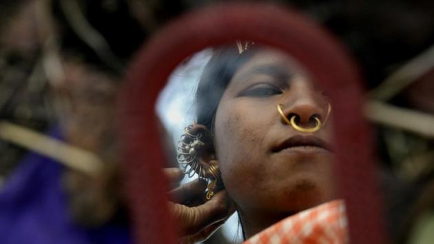 A woman looks at her earrings in front of a mirror. Each member has a unique personal adornment, they use hair clips, earrings neck rings, hand rings made up of brass and iron. (Arabinda Mohapatra) A woman looks at her earrings in front of a mirror. Each member has a unique personal adornment, they use hair clips, earrings neck rings, hand rings made up of brass and iron. (Arabinda Mohapatra)