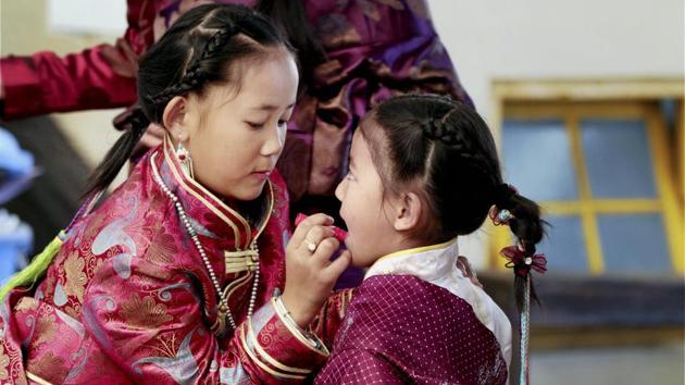 A young Tibetan girl dressed up in traditional attire helps her younger sister get ready on the occasion of the Tibetan New year . (PTI) A young Tibetan girl dressed up in traditional attire helps her younger sister get ready on the occasion of the Tibetan New year . (PTI)