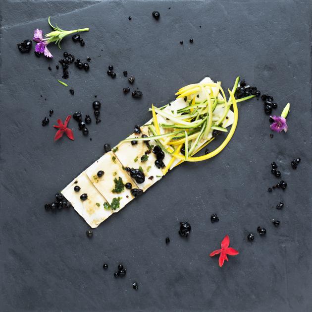 Tofu carpaccio with a soya sauce drizzle and edible flowers, served on slate or stone.