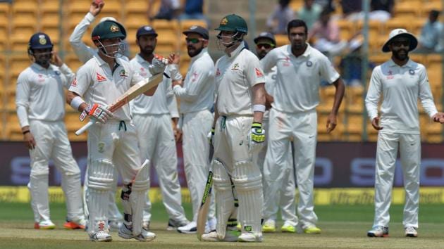 Australian captain Steve Smith (centre), vice captain David Warner, and the Indian team wait for the third umpire's decision on Warner's appeal for a review on his LBW dismissal on Day 4 of the second India vs Australia Test in Bangalore on Tuesday.(AFP)