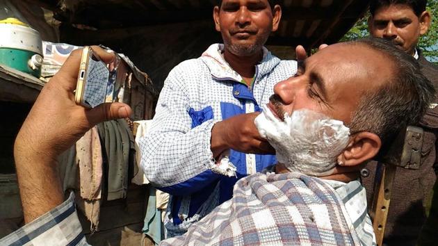 A man watching the election results on his mobile phone as he gets a shave outside a counting centre in Fazilka on Saturday. (Anil Dayal/HT)