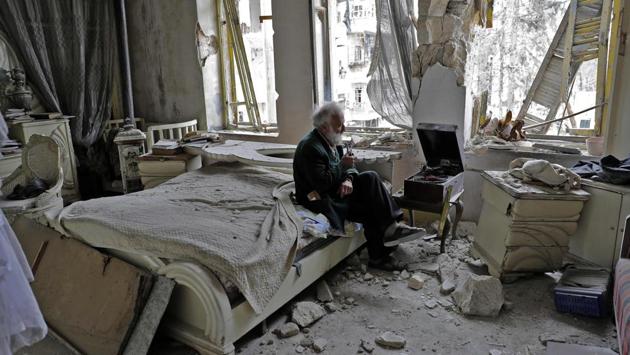 Mohammad Mohiedine Anis, 70, smokes his pipe as he sits in his destroyed bedroom listening to music on his vinyl player in Aleppo's formerly rebel-held al-Shaar neighbourhood. (JOSEPH EID / AFP) 