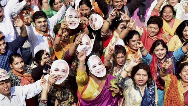 BJP workers and supporters, wearing the mask of Prime Minister Narendra Modi, celebrate the party’s victory in the assembly elections, at party headquarters in New Delhi on Saturday.(PTI Photo)