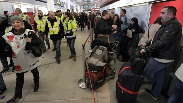 Participants of a strike walk past travellers queuing in front of a booking change counter at the Tegel airport in Berlin.(AP)
