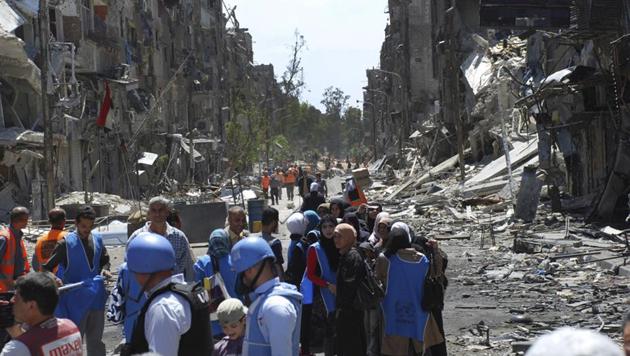 UN relief workers (in blue helmets and vests) wait to receive food aid on the southern edge of the Syrian capital Damascus, Syria, in May 2014. A new investigate report accuses the Syrian government of "slow-motion slaughter" of unknown numbers of Syrians trapped in besieged and hard-to-reach areas by willfully denying them food and health care, which it calls a war crime. (AP File) UN relief workers (in blue helmets and vests) wait to receive food aid on the southern edge of the Syrian capital Damascus, Syria, in May 2014. A new investigate report accuses the Syrian government of "slow-motion slaughter" of unknown numbers of Syrians trapped in besieged and hard-to-reach areas by willfully denying them food and health care, which it calls a war crime. (AP File)