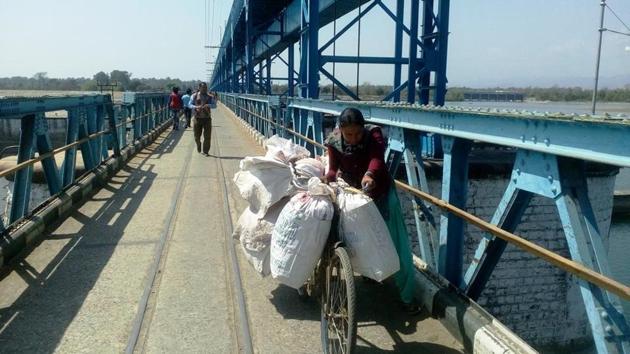 A Nepalese woman pushes her goods laden bicycle on the Sharda barrage at Banbasa.(HT Photo)
