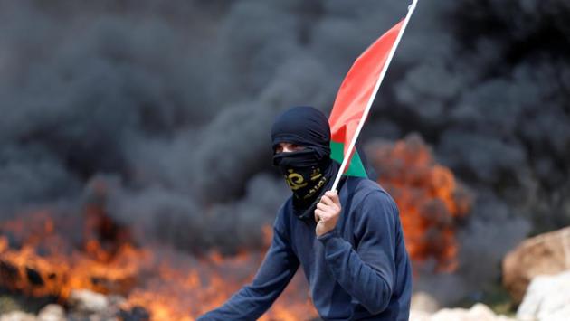 A protester holds a Palestinian flag as smoke rises from burning tyres during clashes with Israeli troops at a protest against Jewish settlements, in al-Mughayyir village near the West Bank city of Ramallah March 24, 2017. (Mohamad Torokman  / REUTERS) 