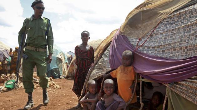 A Somali policeman walks past as newly displaced Somali children stand outside their makeshift shelter at a camp in Baidoa. (Farah Abdi Warsameh/AP)