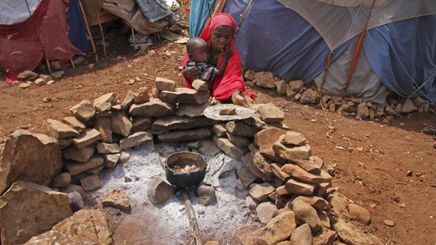 A newly displaced Somali girl holds her sister as they cook food over a fire, next to their makeshift shelter at a camp in Baidoa, Somalia. (Farah Abdi Warsameh/AP)