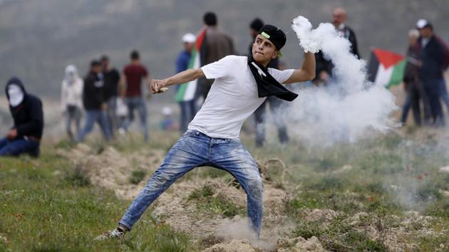 Palestinian youth throws back teargas canister during clashes with Israeli forces following a protest to mark the Land Day near the village of Madama, south of the West Bank city of Nablus. (Majdi Mohammed / AP)