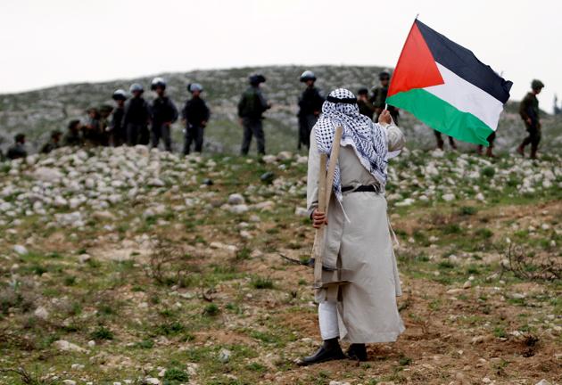 A man holds a Palestinian flag in front of Israeli troops during a protest marking Land Day in the West Bank village of Madama, near Nablus. (Mohamad Torokman / REUTERS)