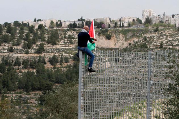 A Palestinian man plants his national flag atop an iron fence, setup by Israeli security forces, between the Palestinian village of Beit Jala and the Jerusalem area, on March 30, 2017 during Land Day protest. (Musa AL SHAERAFP)