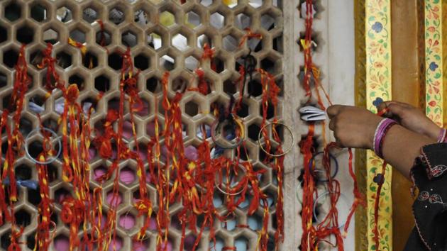 A lady ties sacred thread at a lattice door at the shrine to observe ‘mannat’ or a prayer of belief. (Burhaan Kinu/HT PHOTO)