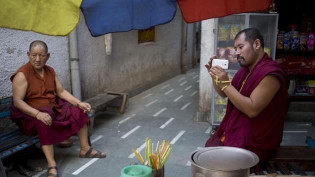 An exile Tibetan monk takes pictures on his mobile sitting outside a temple .The rain, however, followed the Dalai Lama when he arrived at Bomdila’s Lower Gompa after an almost nine-hour drive. (Tsering Topgyal / AP)
