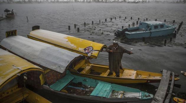 A Kashmiri boatman clears snow from shikara on the shores of the Dal Lake.The snowfall and rains over the past three days have forced the state government to close schools in the Valley till Sunday. (Dar Yasin / AP)
