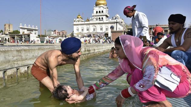 Sikh devotees hold a child as they take a dip in the holy sarovar at Gurudwara Bangla Sahib in New Delhi. (Raj K Raj /ht photo)