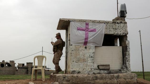 A Iraqi solider stands by a flag with a cross at a check point. Whether more Christians can live permanently in Qaraqosh depends on whether the security forces win their trust. Army and police have tried to ease fears by stationing soldiers in front of churches, and even helping Christian volunteers to set up a massive cross at the town’s entrance. (Marko Djurica/Reuters)