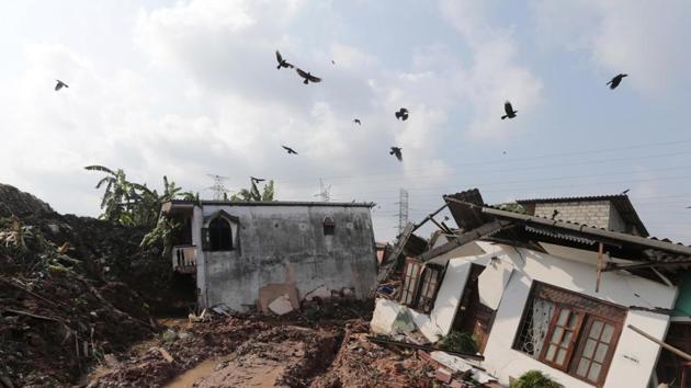 Crows fly over a row of houses buried by a collapse of a garbage dump. (Eranga Jayawardena / AP)