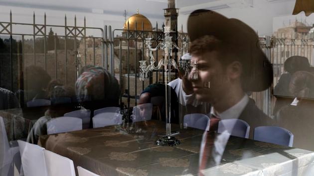 A picture taken through the window of a restaurant on April 13, 2017 shows a reflection of Jewish people taking part in the Cohanim prayer (priest's blessing) during the Passover (Pesach) holiday at the Western Wall in the Old City of Jerusalem, with the Dome of the Rock seen in the background. Thousands of Jews make the pilgrimage to Jerusalem during the eight-day Pesach holiday, which commemorates the Israelites' exodus from slavery in Egypt some 3,500 years ago and their plight by refraining from eating leavened food products. (Thomas COEX / AFP)