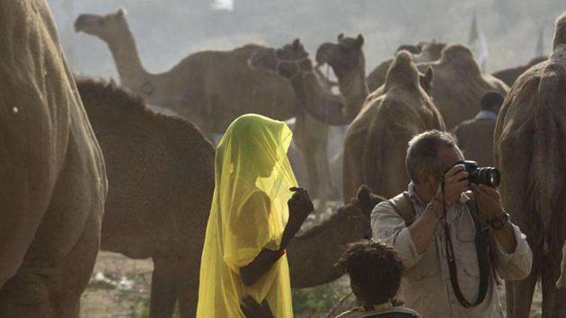 A woman walks past camels as a foreign tourist takes pictures at the Pushkar fair in Pushkar, Rajasthan. Pushkar, located on the banks of Pushkar Lake, is a popular Hindu pilgrimage spot that is also frequented by foreign tourists for its annual cattle fair and camel races.(HT FILE PHOTO)