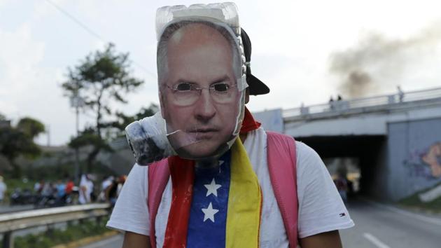 An anti-government protester wears a mask with the image of jailed opposition leader Antonio Ledezma. The conservative-led opposition says government incompetence is to blame and calls the elected president a dictator. It wants early elections. But Maduro, who has the backing of the armed forces, says Venezuela is the victim of a US-led capitalist plot. (Ariana Cubillos/AP) An anti-government protester wears a mask with the image of jailed opposition leader Antonio Ledezma. The conservative-led opposition says government incompetence is to blame and calls the elected president a dictator. It wants early elections. But Maduro, who has the backing of the armed forces, says Venezuela is the victim of a US-led capitalist plot. (Ariana Cubillos/AP)
