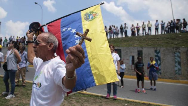 A man holds a crucifix and a Venezuelan flag as anti-government protesters block a highway in Caracas. Thousands of protesters shut down the capital city's main highway to express their disgust with the socialist administration of President Nicolas Maduro. Protesters in least a dozen other cities also staged sit-ins as the protest movement is entering its fourth week. (Fernando Llano/AP) A man holds a crucifix and a Venezuelan flag as anti-government protesters block a highway in Caracas. Thousands of protesters shut down the capital city's main highway to express their disgust with the socialist administration of President Nicolas Maduro. Protesters in least a dozen other cities also staged sit-ins as the protest movement is entering its fourth week. (Fernando Llano/AP)