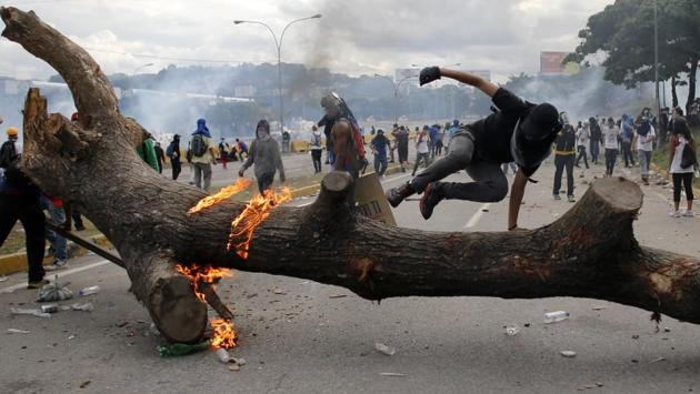 A demonstrator jumps over a tree trunk set by protesters as a barricade . (Ariana Cubillos / AP)