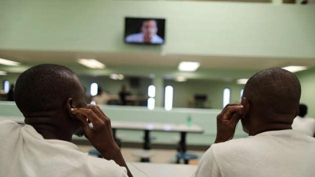 Men share a pair of headphones to watch television in a dormitory. At the facility, some of the detainees could be seen chatting over meals of rice and refried beans, while others sat alone in silence. Two men shared a pair of headphones to watch television, and others played dominoes. (Lucy Nicholson /Reuters)
