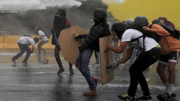 Anti-government protesters take cover from a water canon fired by security forces blocking a student march from reaching the Education Ministry. (AP)