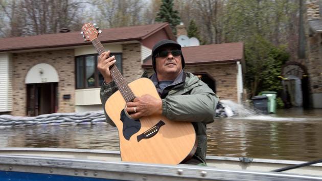 A man plays his guitar as he travels in a boat to collect water supplies in a flooded residential neighbourhood in Ile Bizard. (Christinne Muschi/REUTERS)