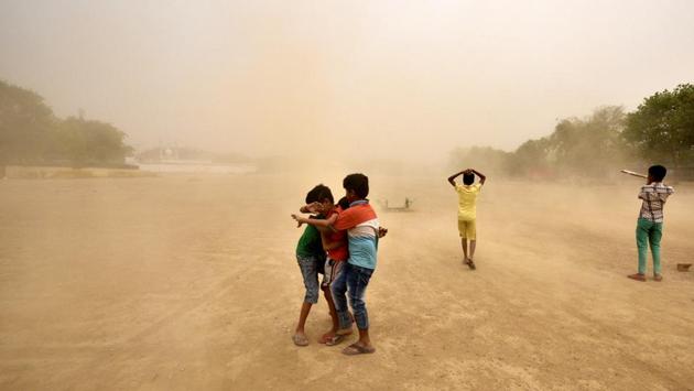 Children  try  to protect themselves from  a dust storm . Dry weather had resulted in occasional dust storms across the northern region. (Arun Sharma/HT PHOTO) 