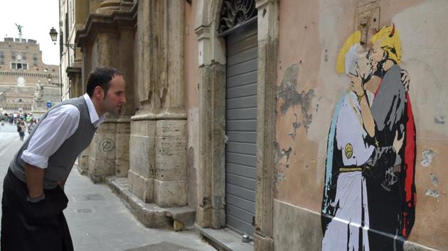 A waiter looks at a collage showing Pope Francis kissing US President Donald Trump near Castel Sant'Angelo in central Rome.(AFP Photo/Andreas Solaro)