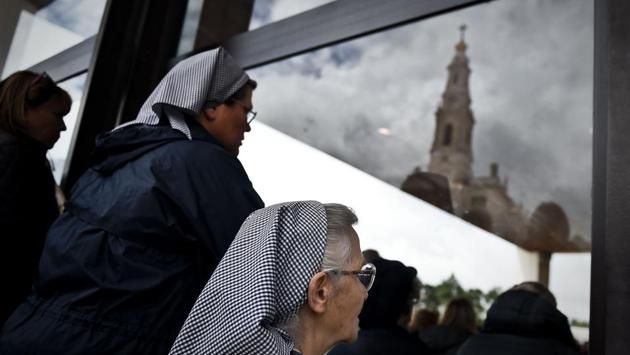 Two nuns outside the chapel "Capelinha das Aparicoes" attend a mass as the "Nossa Senhora do Rosario de Fatima" cathedral's spire is reflected on the window at Fatima. (Patricia De Melo Moreira/AFP)