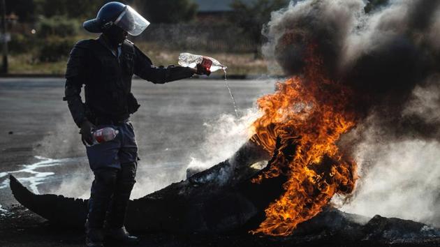 A South African policeman attempts to extinguish a fire after demonstrators burnt tyres to barricade a road, during violent protest demanding better housing in Finetown, Ennerdale, South Africa. (MUJAHID SAFODIEN / AFP)