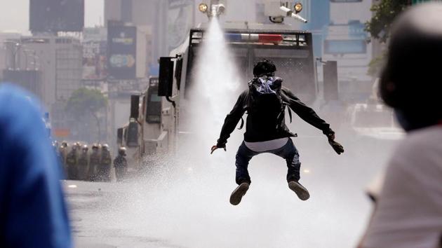 A demonstrator jumps away from a jet of water released from a riot security forces vehicle during a rally against Venezuela's President Nicolas Maduro in Caracas, Venezuela. (Carlos Barria / REUTERS)