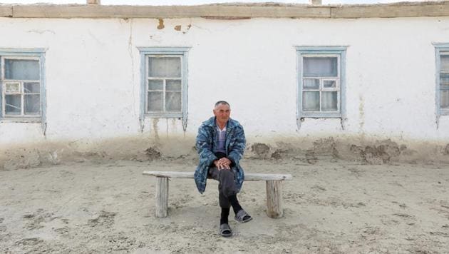 Erali Serimbetov, who was born in 1961, sits in front of his house surrounded by dunes at the remote part of the village of Karateren. (Shamil Zhumatov / REUTERS) 