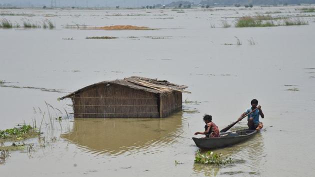 A boy rows a boat past a submerged hut in a flooded field at Mayong village. (Anuwar Hazarika / REUTERS)
