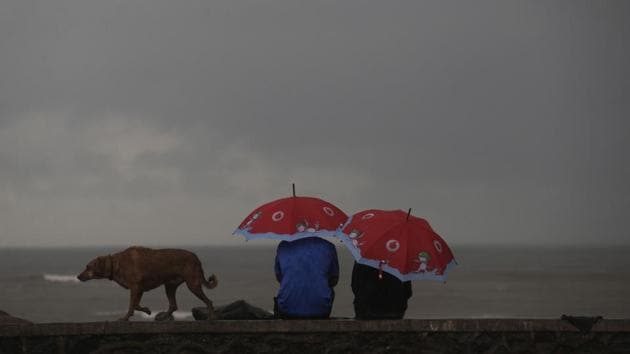 Indians sit holding umbrellas on the Arabian sea coast during monsoon rains as a dog walks past in Mumbai.(AP Photo)