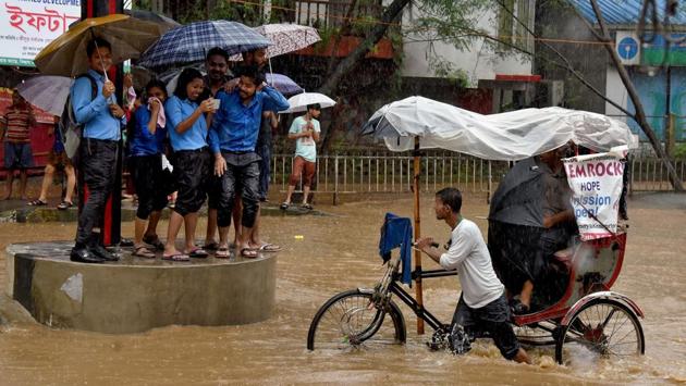 College students take shelter at a traffic point as a man paddles his rickshaw through a flooded street. (REUTERS) College students take shelter at a traffic point as a man paddles his rickshaw through a flooded street. (REUTERS)