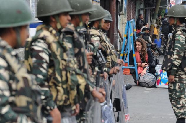 An international tourist sits on the road as Indian paramilitary troops stand guard in Darjeeling on June 18, 2017, following a day of clashes with supporters of the separatist Gorkha Janmukti Morcha (GJM) group. Hundreds of protesters on June 18 paraded with coffins containing the bodies of two men they claimed were killed in clashes with Indian security forces in Darjeeling, as the hill resort reels from separatist unrest. / AFP PHOTO / DIPTENDU DUTTA (AFP) An international tourist sits on the road as Indian paramilitary troops stand guard in Darjeeling on June 18, 2017, following a day of clashes with supporters of the separatist Gorkha Janmukti Morcha (GJM) group. Hundreds of protesters on June 18 paraded with coffins containing the bodies of two men they claimed were killed in clashes with Indian security forces in Darjeeling, as the hill resort reels from separatist unrest. / AFP PHOTO / DIPTENDU DUTTA (AFP)