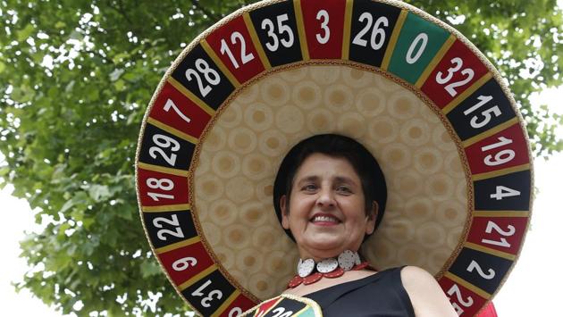 A racegoer wears a hat based on a roulette wheel. (Alastair Grant / AP) A racegoer wears a hat based on a roulette wheel. (Alastair Grant / AP)