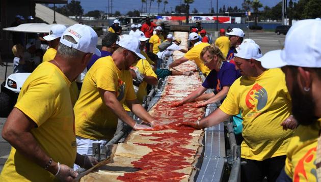 Volunteers spread tomato sauce and cheese onto the pizza base as they successfully break the Guinness World Record for the longest pizza in Fontana, California.(AFP) Volunteers spread tomato sauce and cheese onto the pizza base as they successfully break the Guinness World Record for the longest pizza in Fontana, California.(AFP)