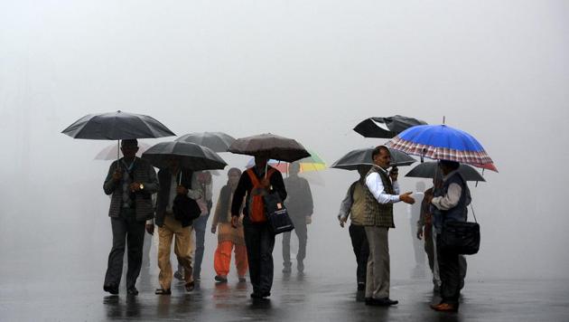 People walking through the dense fog with umbrellas during heavy rainfall at the Ridge, Shimla, on Wednesday. (Deepak Sansta/HT Photo)